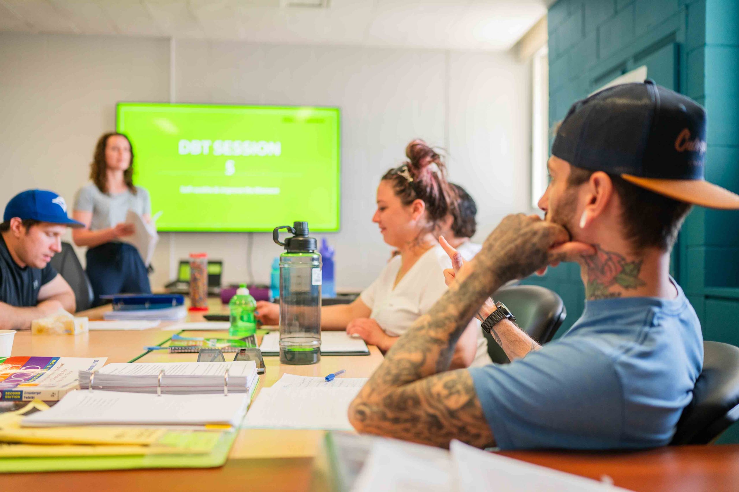 A group of people sitting around a table in a board room in a mental health centre and listening to a presentation.