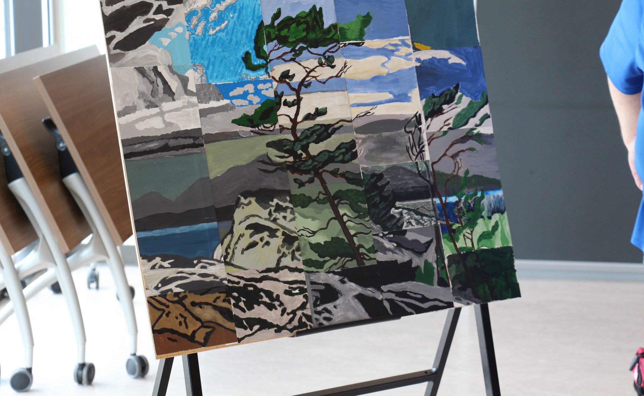 An easel holding an abstract painting of a tree in a mountain setting.