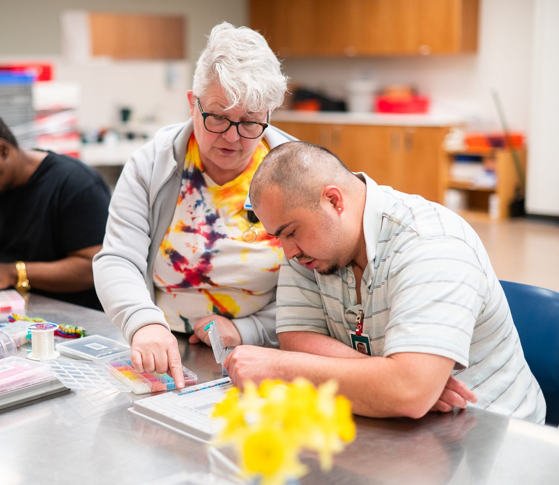 An instructor helps a man with an art activity at a table.