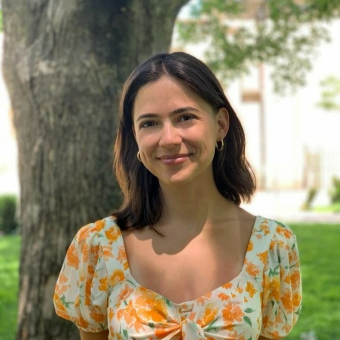 A headshot of Arina Bogdan smiling and standing in front of a tree.
