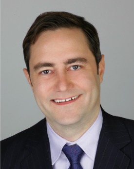 A headshot of Dr. Kolla smiling in front of a grey background.