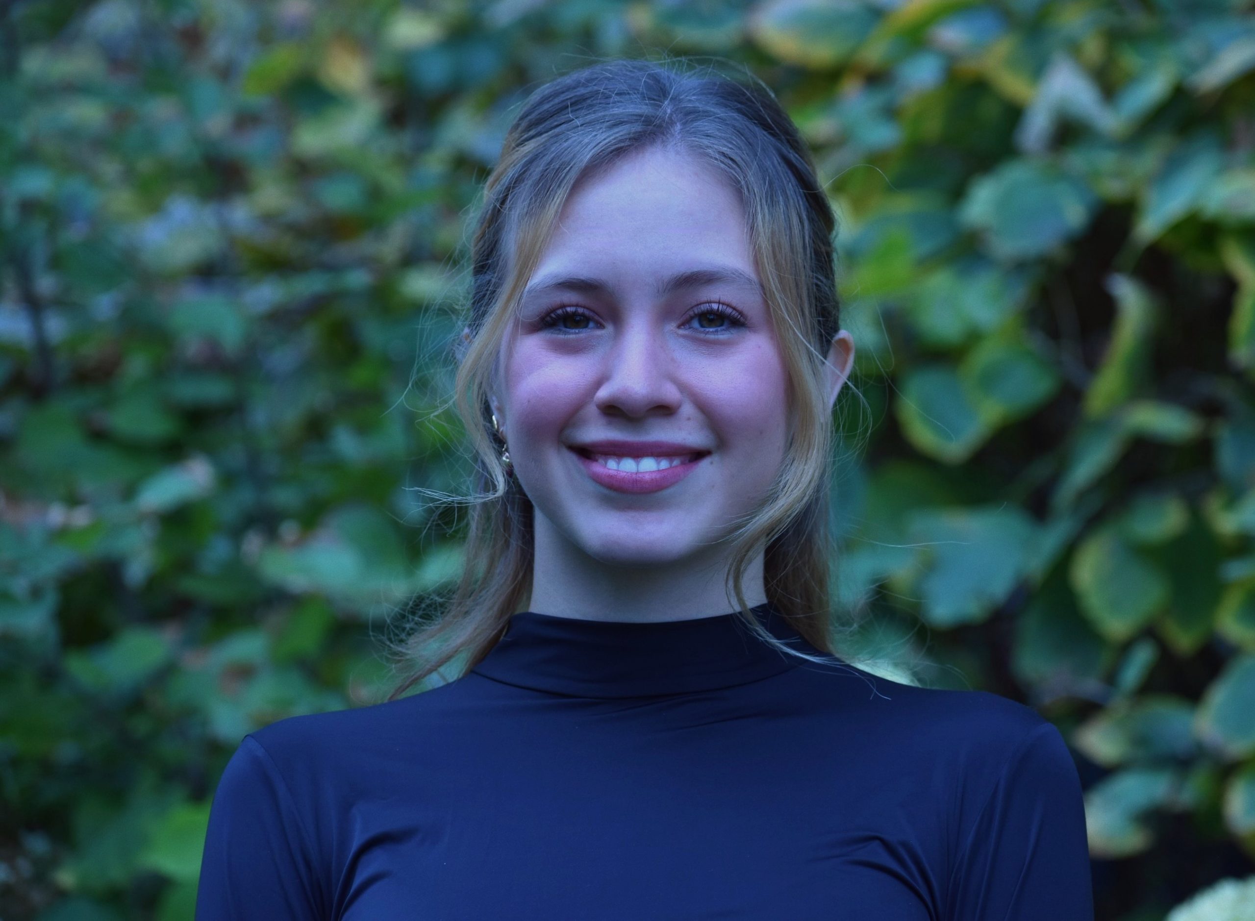 A staff headshot of Valentina Tamayo smiling and standing in front of a green bush.